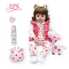 A baby doll wearing a pink outfit with a pink jacket and pink accessories, next to various small decorative items.