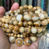 A handful of natural gemstone beads in various shades of brown and tan, including tiger eye and lava stones.