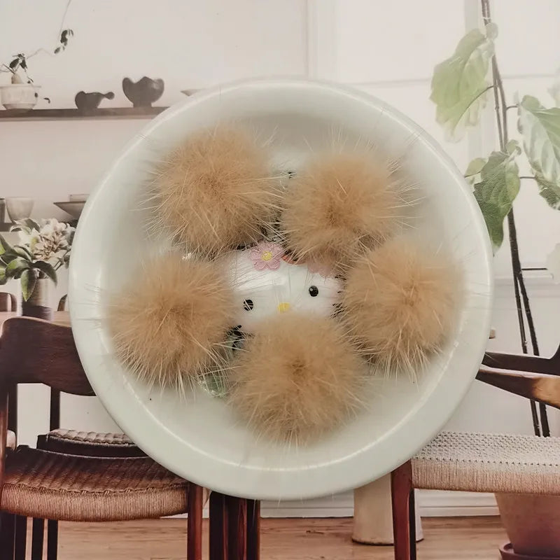 A white bowl filled with several fluffy, light brown mink fur pom poms for crafts and accessories.
