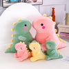 A collection of soft plush dinosaur toys in shades of green and pink sitting on a white surface.