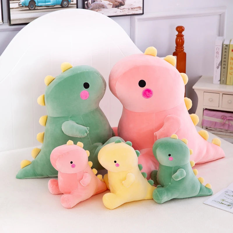 A collection of soft plush dinosaur toys in shades of green and pink sitting on a white surface.