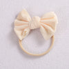 A pale peach or cream colored fabric bow headband with a soft elastic band.
