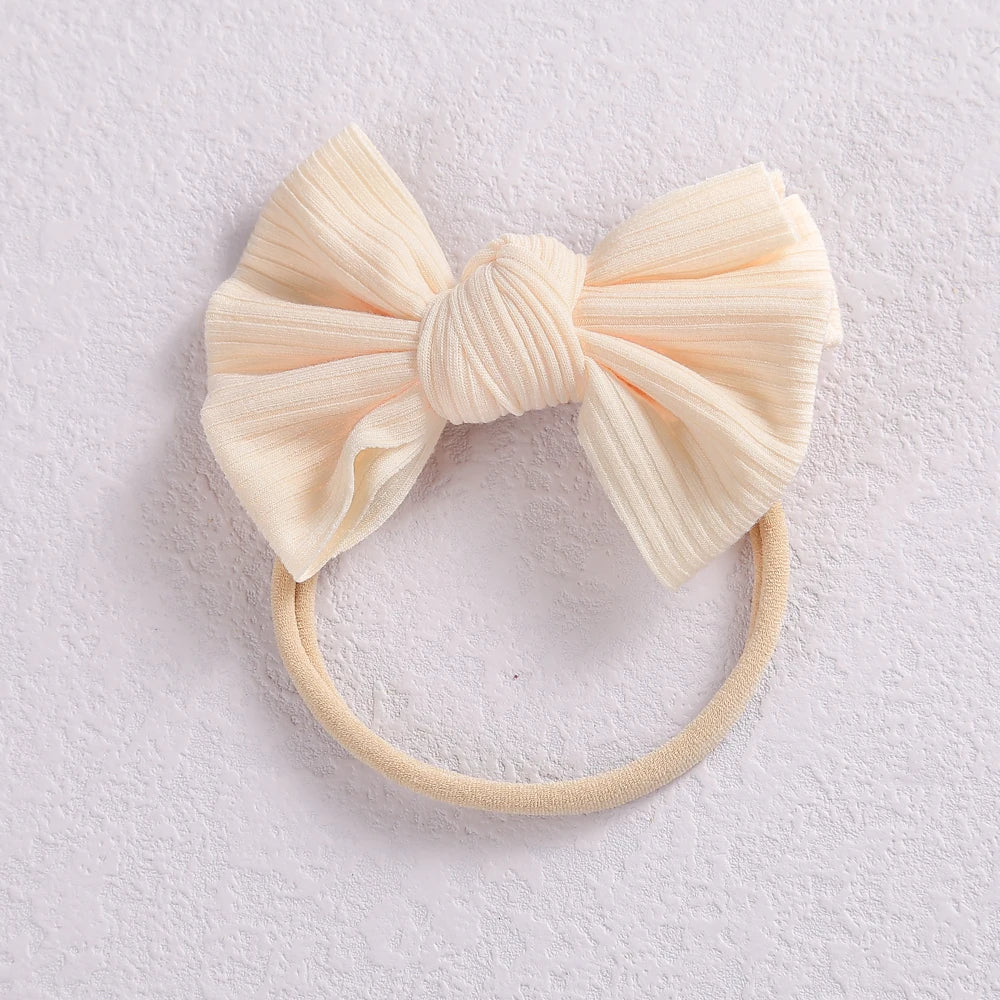 A pale peach or cream colored fabric bow headband with a soft elastic band.