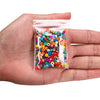 A hand holds a small clear plastic bag filled with various colored round glass seed beads for jewelry making