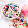 A bowl filled with a colorful mix of assorted pearl beads in various shades including pink, blue, green, and gold.