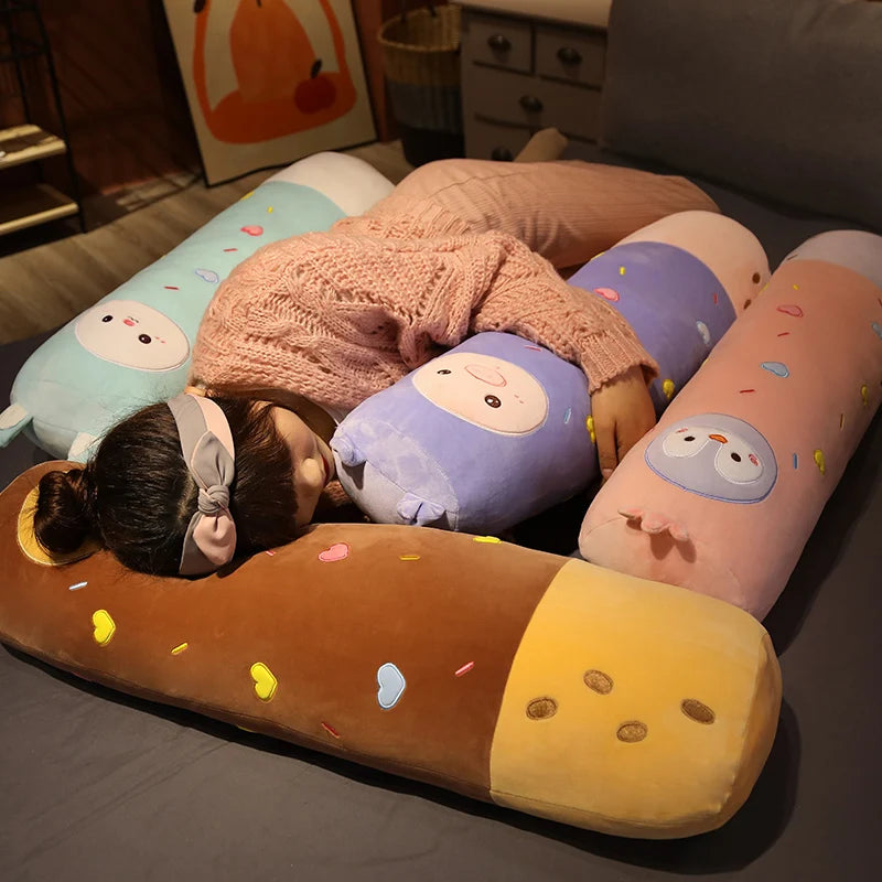 A long body stuffed animal plush pillow in orange and yellow with colorful sprinkles resting on a dark surface.