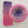 A ball of rainbow gradient mercerized cotton cake yarn showing pink and purple hues.