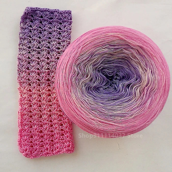 A ball of rainbow gradient mercerized cotton cake yarn showing pink and purple hues.