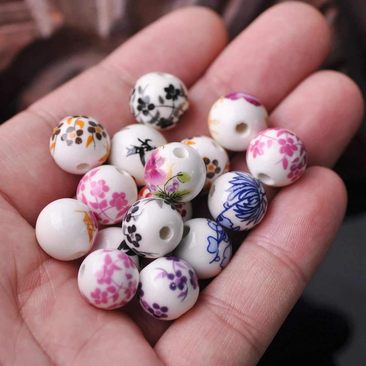 A hand holds a collection of white ceramic beads decorated with floral patterns in various colors and shades.