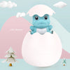 A cute blue dinosaur toy in a white egg with surrounding clouds and a small green tree.