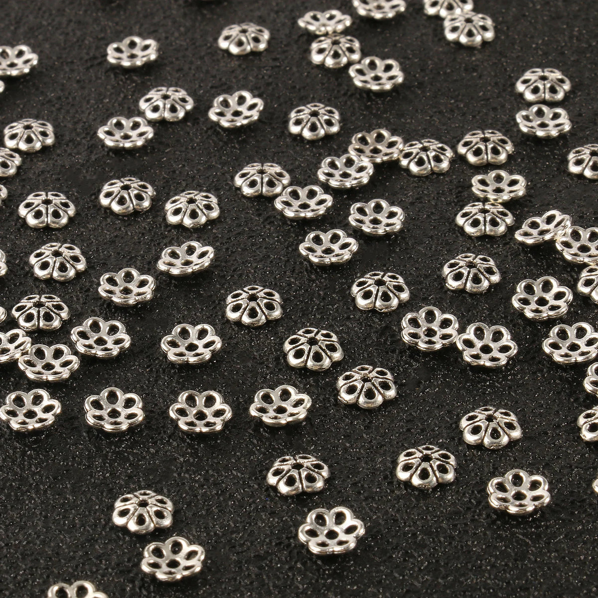 Small silver hollow flower bead caps scattered on a black surface for jewelry making