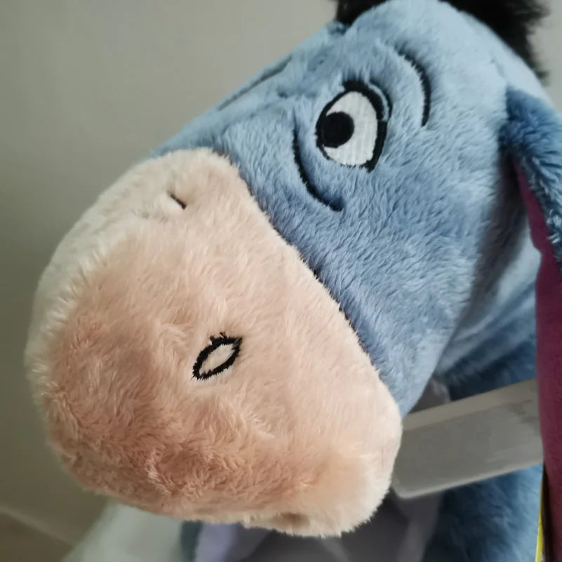 A close-up of an Eeyore plush toy, a soft blue donkey stuffed animal with a pink muzzle.