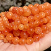 A pile of small, round, translucent orange-red gemstone beads for jewelry making.