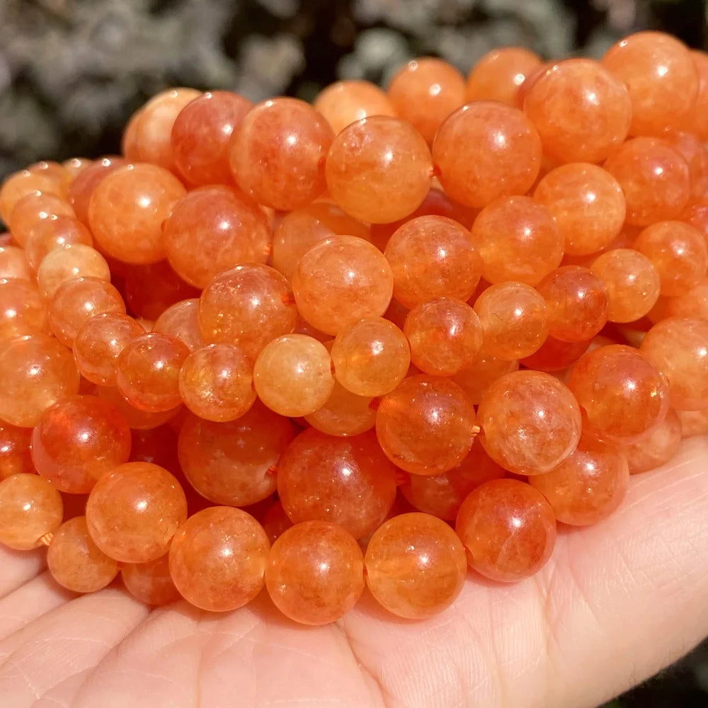 A pile of small, round, translucent orange-red gemstone beads for jewelry making.