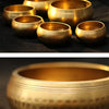 Several handmade copper singing bowls of varying sizes are displayed on a dark surface.