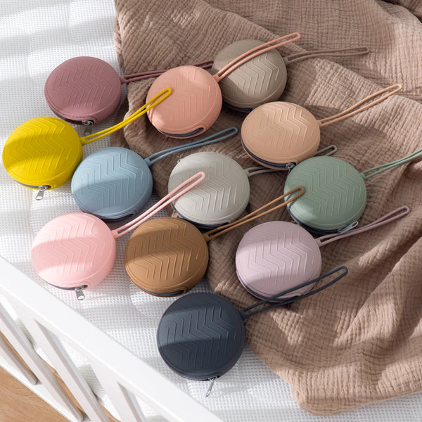 A collection of soft silicone pacifier holders in various pastel colors resting on a beige knitted fabric.