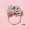 A beige ribbed fabric bow headband is displayed against a pink background.