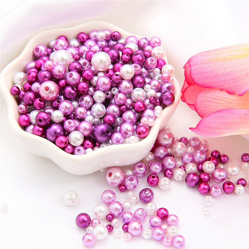 A pile of assorted purple and pink pearl beads for jewelry making displayed on a white surface.