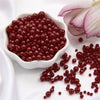 A pile of small, reddish-brown pearl beads scattered on a white surface.