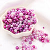 A pile of assorted purple and white pearl beads in a white dish.