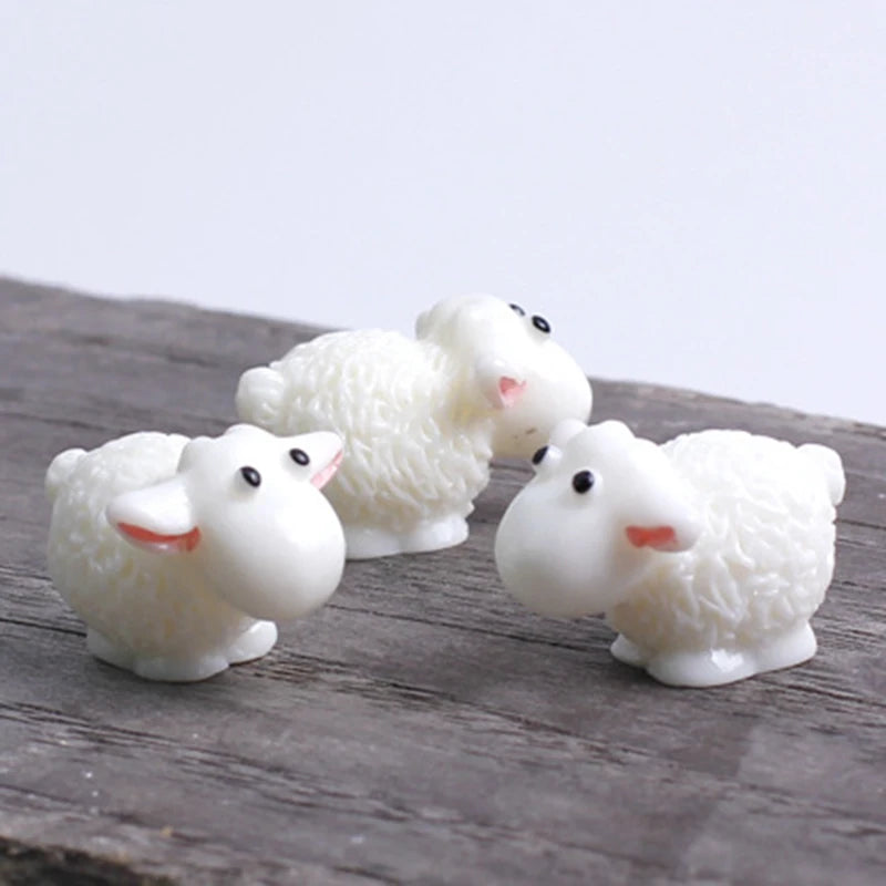 Three white miniature sheep figurines with pink ears resting on a dark wooden surface.