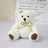 A white patch bear plush toy with brown nose and a yellow ribbon, sitting on a white surface.