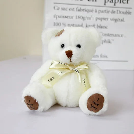 A white patch bear plush toy with brown nose and a yellow ribbon, sitting on a white surface.