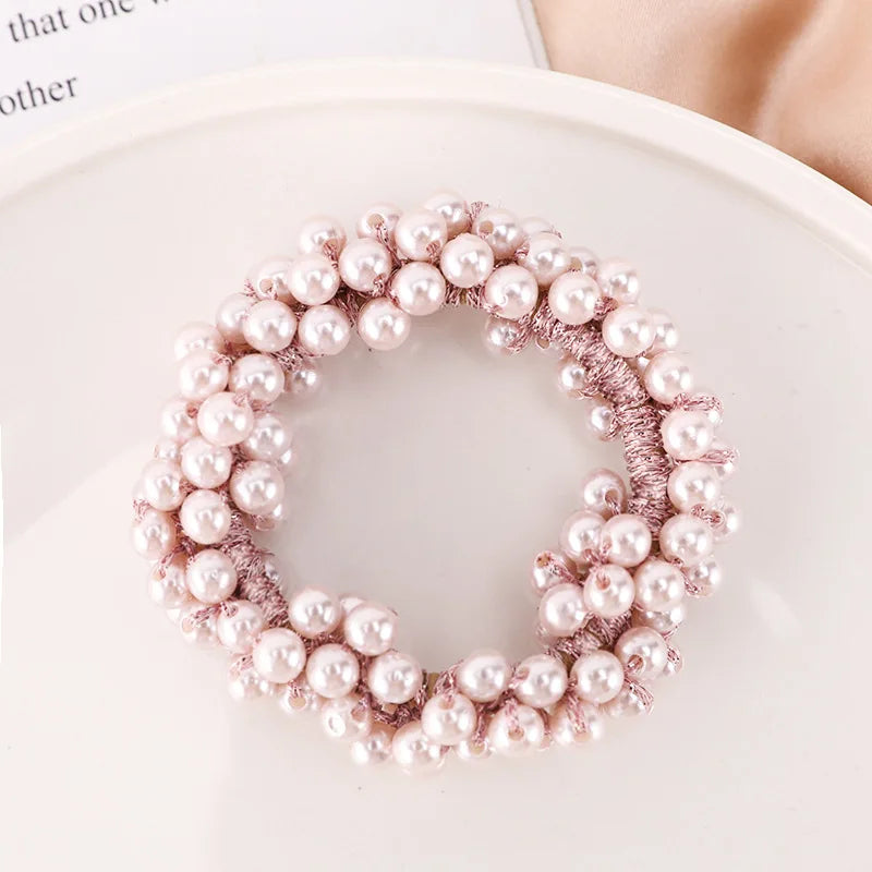A circular arrangement of pink pearl hair ties with bows and scrunchies on a white plate.