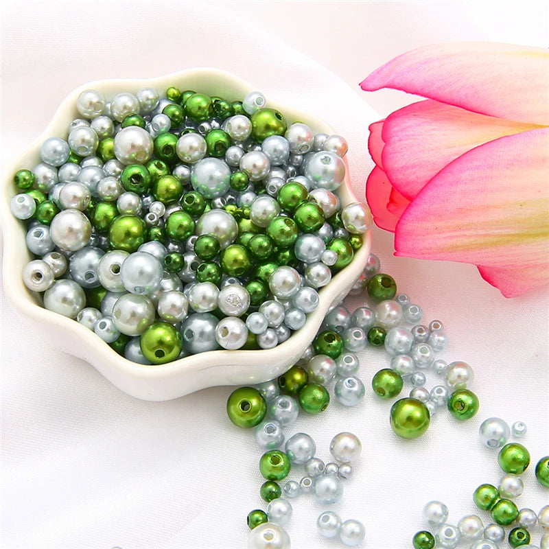 A bowl filled with assorted green and silver pearl beads next to a pink lotus flower.