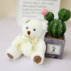 A white patch bear plush toy with a yellow bow and a small green cactus plant in a gray pot.