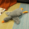 A gray oversized kawaii goose plush pillow with orange beak and feet resting on a light yellow and blue textured surface.