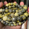 A hand holds a collection of natural gemstone beads in various shades of yellow, green, and black.