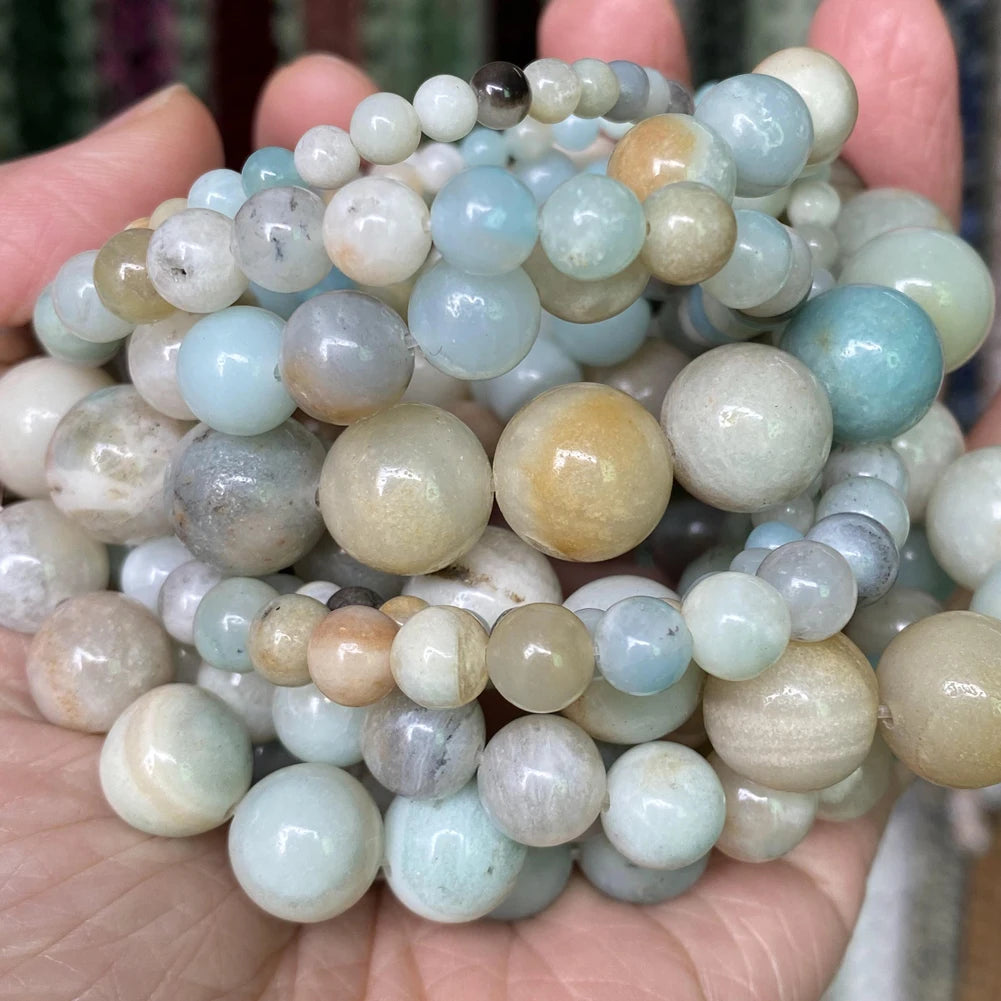 A collection of round natural gemstone beads in shades of blue, green, and beige are held in a person's hand.