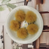 A white bowl filled with several fluffy yellow mink fur pom poms for crafts and accessories.