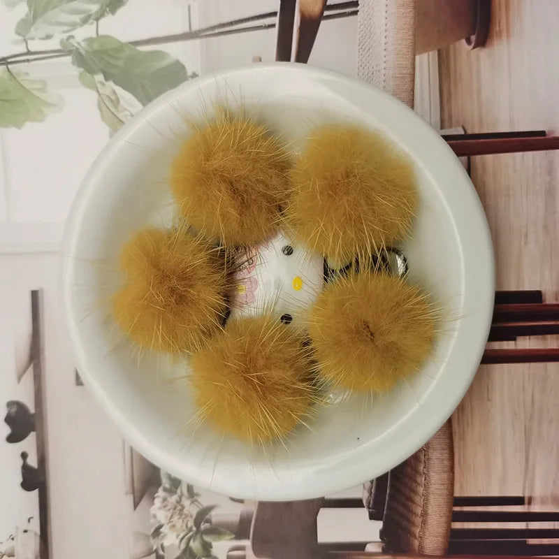 A white bowl filled with several fluffy yellow mink fur pom poms for crafts and accessories.