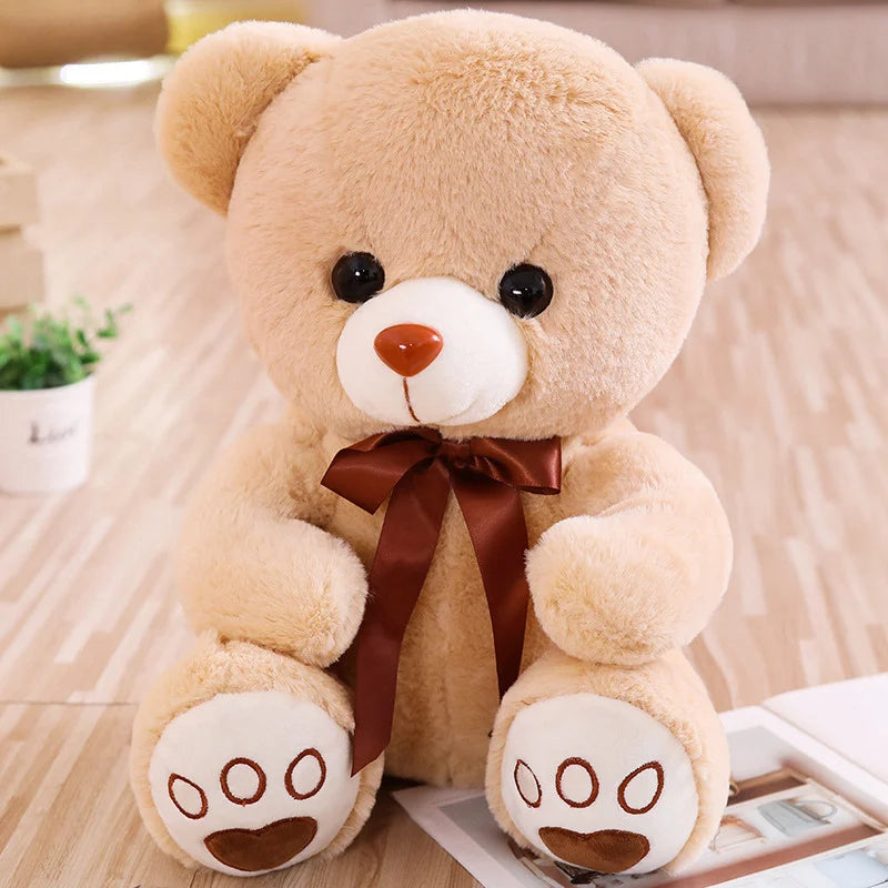 A light tan plush teddy bear with brown accents sitting on a wooden surface.