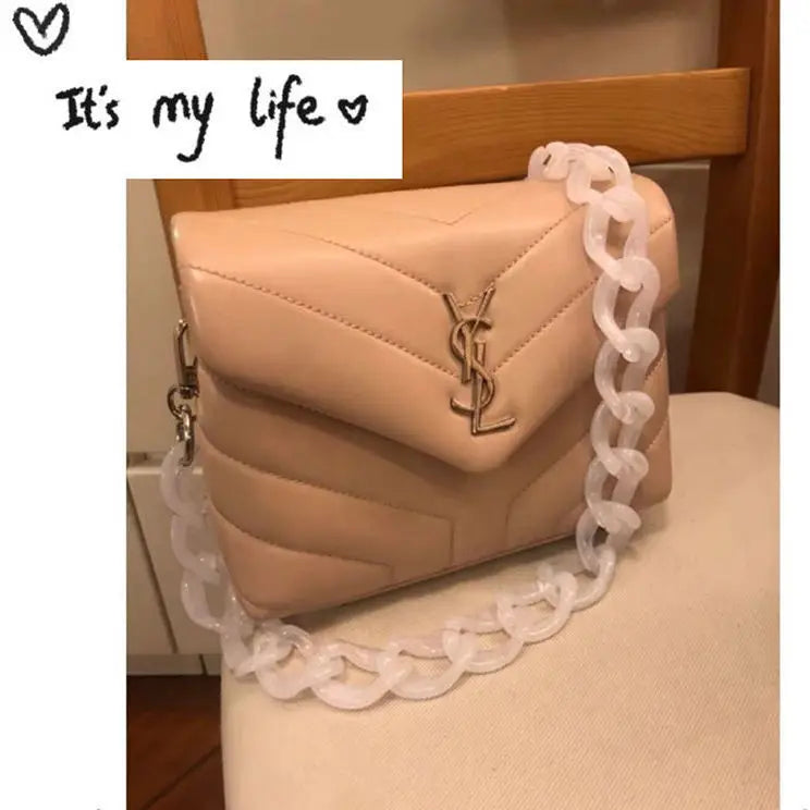 A light pink acrylic bag featuring a gold logo and adorned with a clear beaded chain strap.