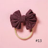 A dark purple textured bow headband with a light yellow elastic band against a pink background.