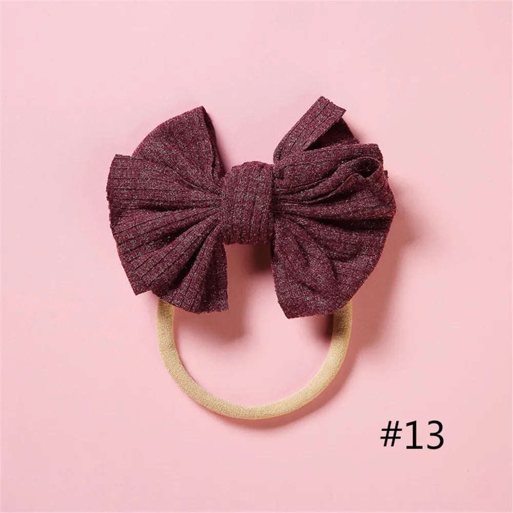 A dark purple textured bow headband with a light yellow elastic band against a pink background.