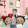 A young woman is holding two plush toys shaped like black and yellow ladybugs or bees against a pink striped background.