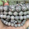 A hand holds a string of natural gemstone beads including tiger eye, lava, and turquoise for jewelry making.