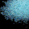 A pile of small, iridescent blue and purple glass bubble beads scattered against a black background.