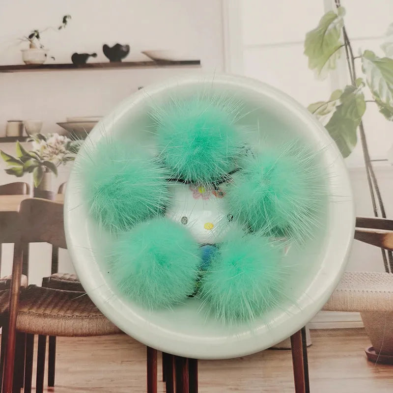 A bowl filled with bright turquoise green faux fur pom poms for crafting and accessories.