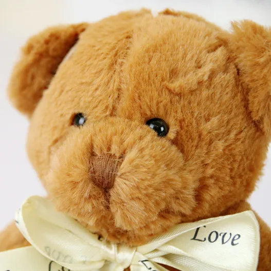 A fluffy brown patch bear plush toy with a cream ribbon tied around its neck.
