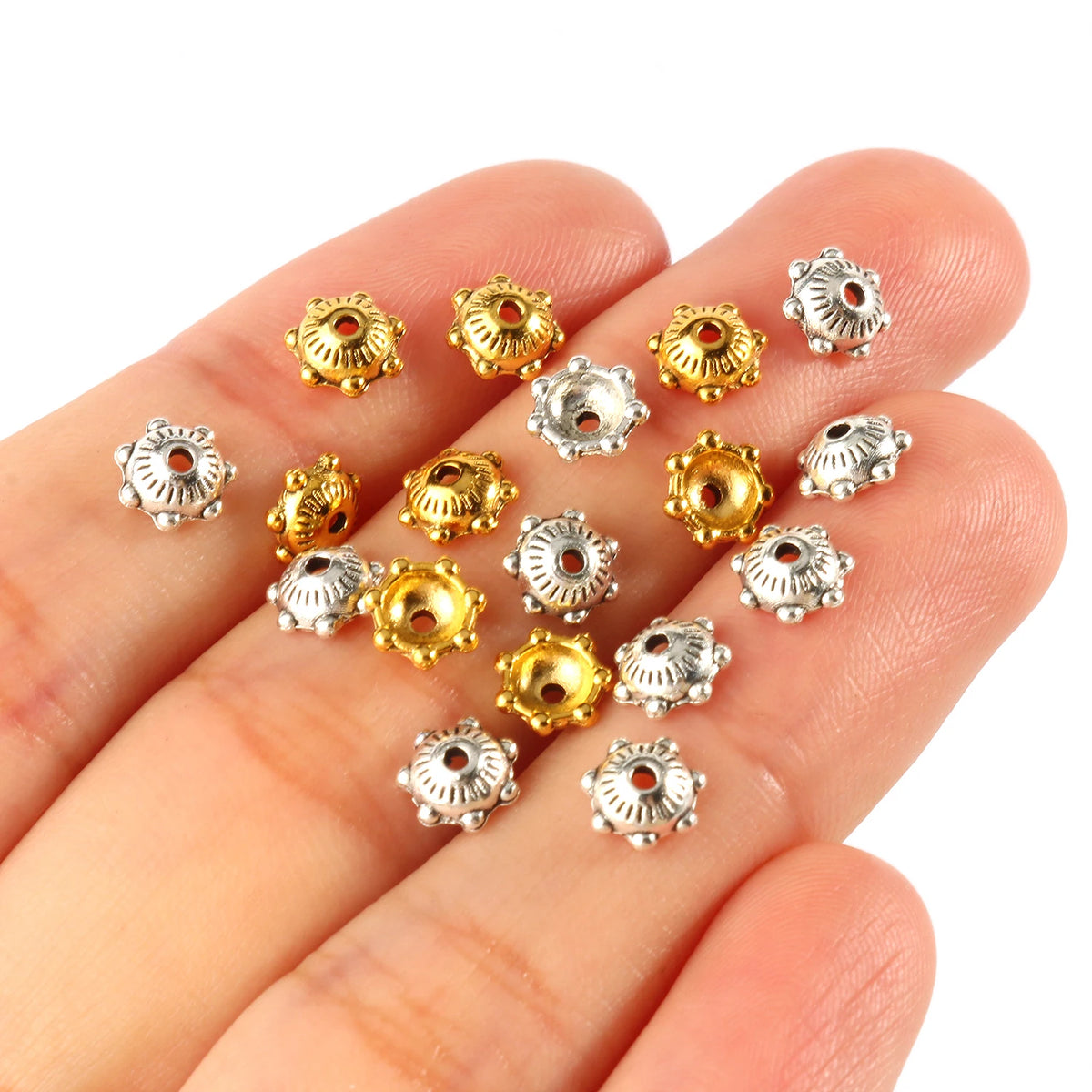 A hand holds several small, gold and silver Tibetan style hollow flower bead caps for jewelry making.