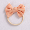 A soft peach knitted bow headband with a light beige elastic band.