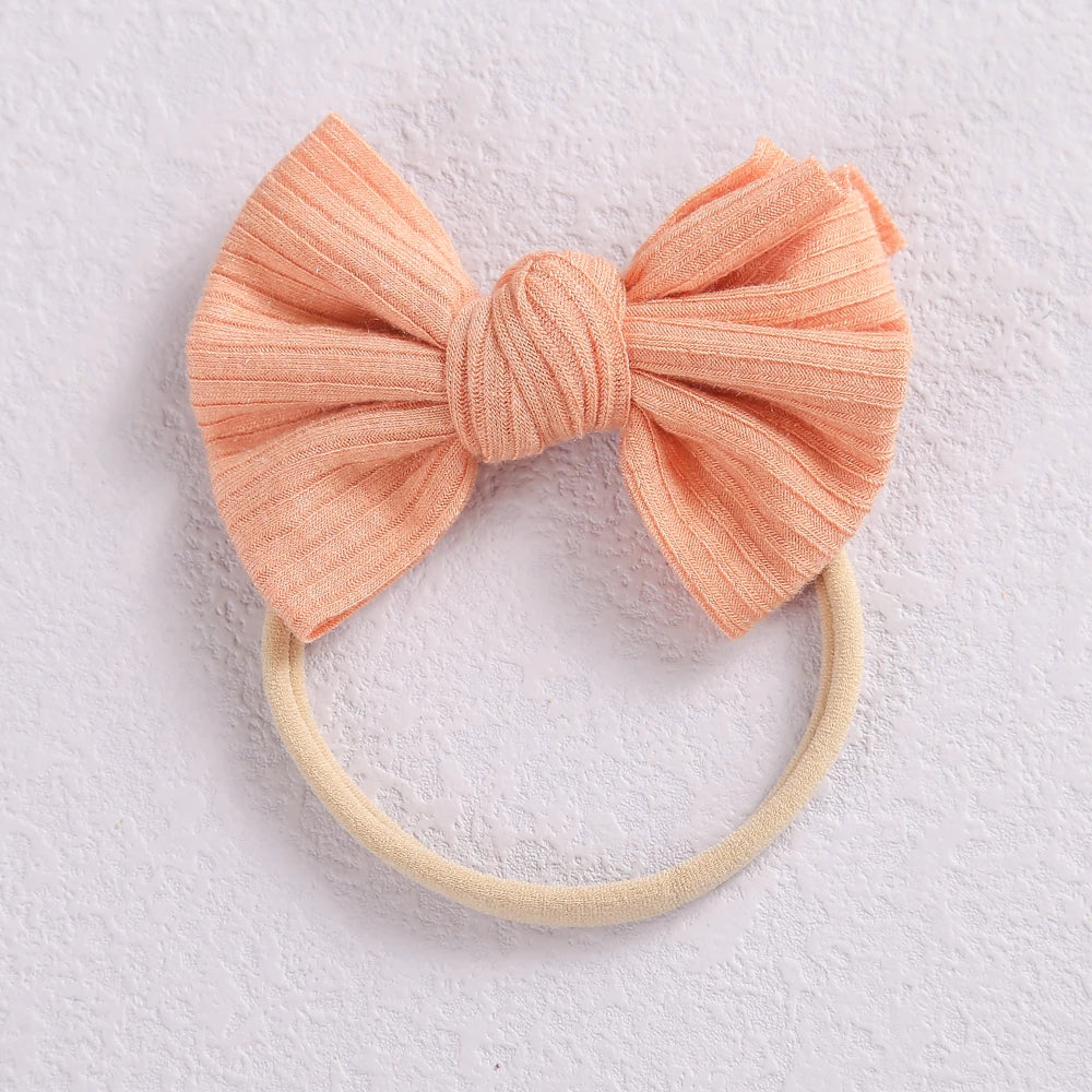A soft peach knitted bow headband with a light beige elastic band.