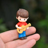 A small figurine of a boy playing a yellow guitar, held in a person's hand.