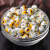A bowl filled with small white ceramic beads decorated with yellow and blue floral patterns for jewelry making