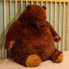 An oversized, lifelike brown bear plush cushion sitting on a light surface against a wooden background.